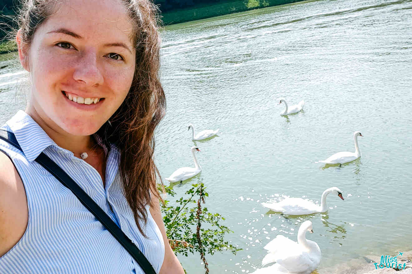 Woman smiling by a lake with six swans swimming in the water.