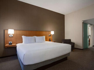 A hotel room with a large bed, two bedside lamps, a dark armchair, and neutral-colored walls and carpet.