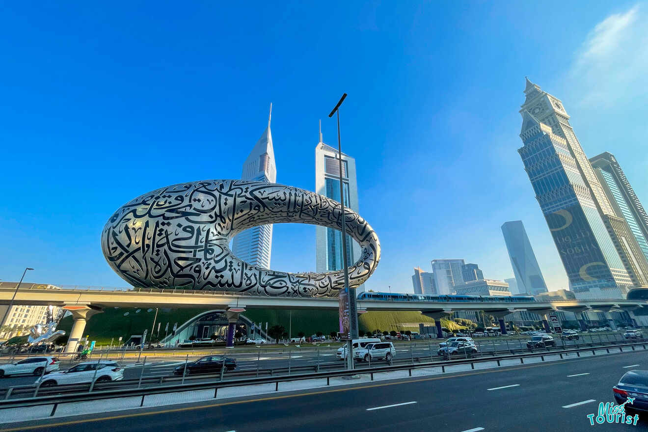 Futuristic building with Arabic calligraphy, skyscrapers in the background, and a highway in the foreground under a clear blue sky.