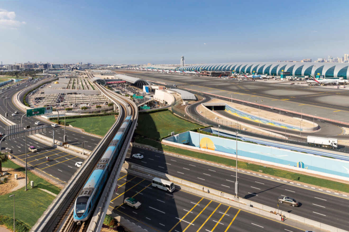 An aerial view of a large airport and its surroundings, featuring multiple runways, terminals, a train on elevated tracks, and adjacent roads with vehicles.