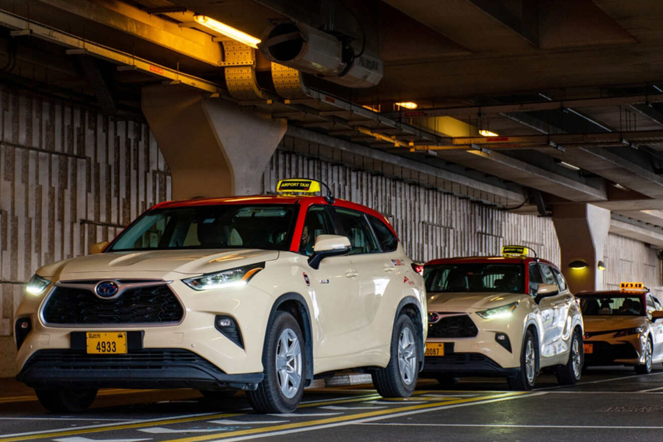 Line of beige taxis with yellow roof signs parked under a concrete ceiling.