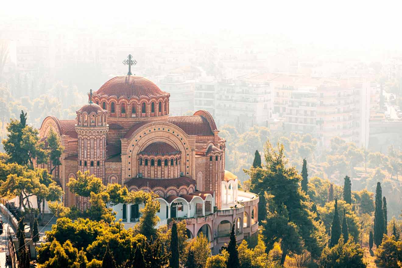 A red-domed church is surrounded by trees with a hazy cityscape in the background.