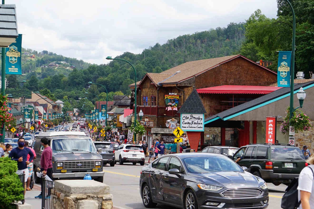 Busy street scene in a mountain town with cars, pedestrians, shops, and greenery.