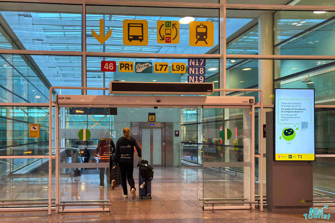 Passengers walking through an airport terminal entrance with various signs for bus and train connections overhead.