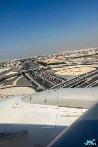 View from an airplane window showing engine and a busy highway below, with cars and surrounding desert landscape.