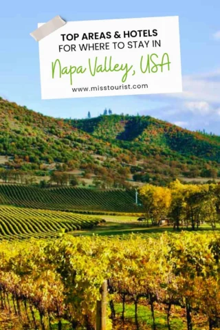 Scenic view of a vineyard in Napa Valley, with rolling green hills under a blue sky. A sign promotes "Top Areas & Hotels for Where to Stay in Napa Valley, USA.