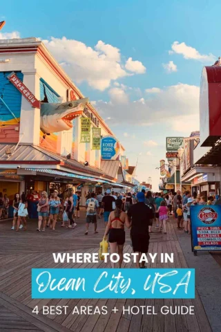 A crowded boardwalk in Ocean City, USA, with shops and a shark model overhead. Text at the bottom reads: "Where to stay in Ocean City, USA: 4 best areas + hotel guide.