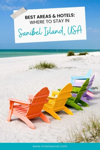 Four colorful Adirondack chairs face the ocean on a sandy beach under a clear blue sky. A sign reads 