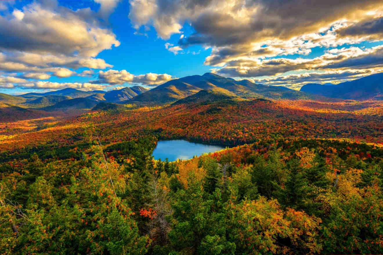 Aerial view of a mountainous landscape with a lake surrounded by vibrant autumn foliage under a partly cloudy sky.