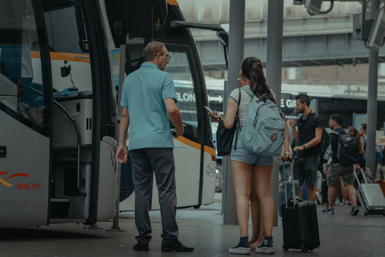 People with luggage standing near a bus at a station.