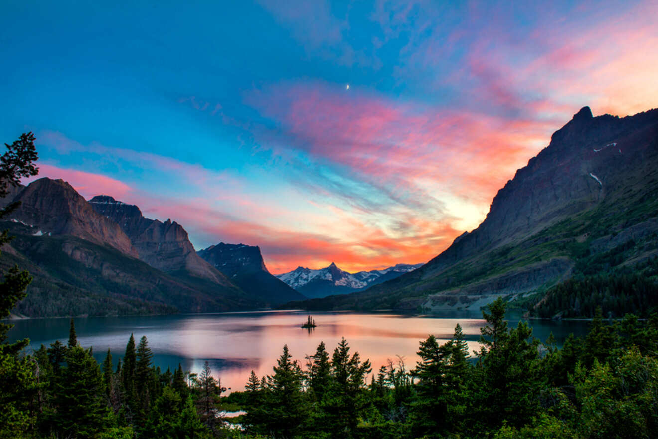 A serene lake surrounded by mountains at sunset, with colorful pink, orange, and blue hues in the sky.