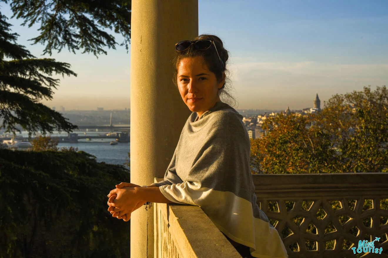 author of the post leans against a railing on a balcony, overlooking a cityscape with a river and distant buildings at sunset.