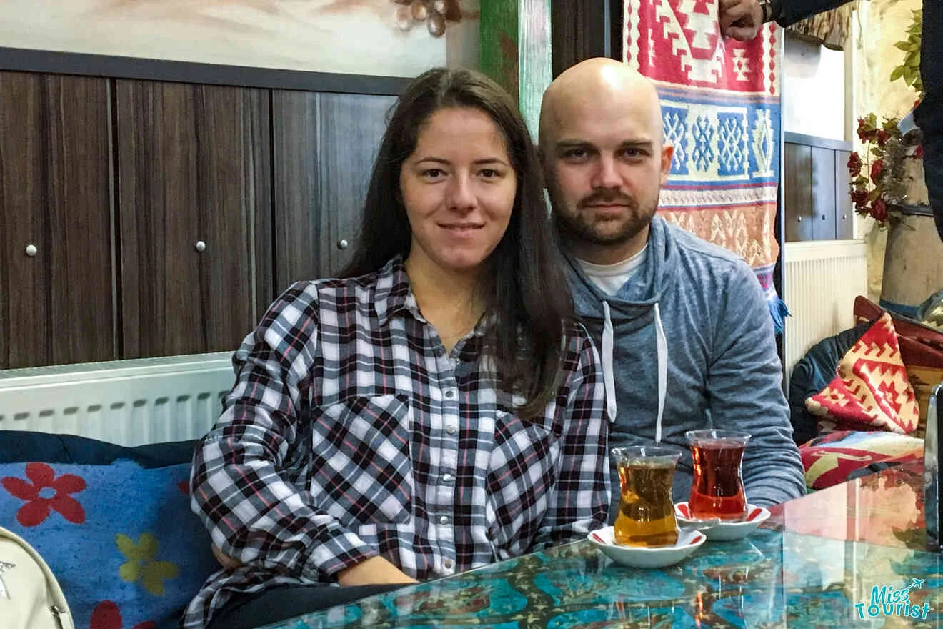 The writer of the post with her husband sitting at a table in a cozy room with patterned fabrics, enjoying tea from traditional glasses.