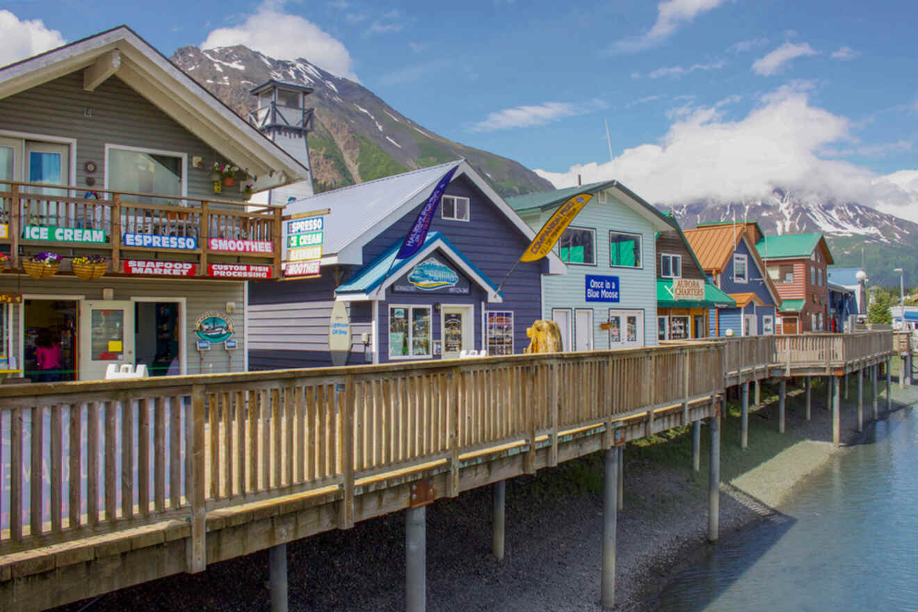 Colorful row of shops on a wooden boardwalk by the water, with mountains in the background under a blue sky.