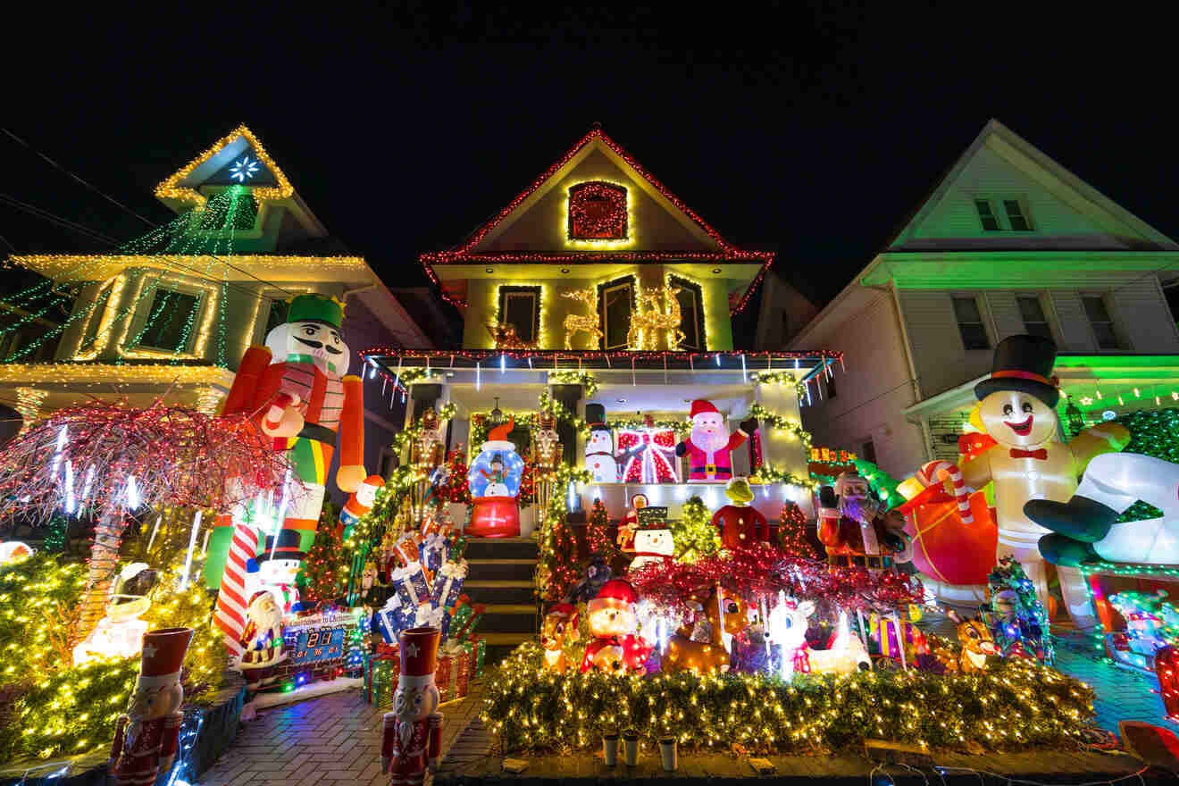 A brightly decorated house with numerous Christmas lights, inflatable figures, and holiday ornaments, including a large nutcracker and snowman, creates a festive nighttime display.