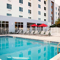 Outdoor swimming pool with lounge chairs and red umbrellas in front of a multi-story building.