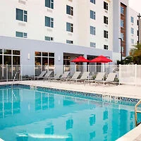 Outdoor swimming pool with lounge chairs and red umbrellas in front of a multi-story building.