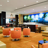 A modern hotel lobby with orange and beige chairs, a large palm tree mural, and overhead lighting.