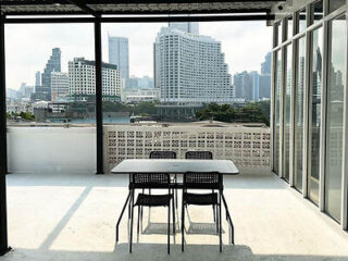 Outdoor terrace with a table and three chairs overlooking a cityscape with modern high-rise buildings in the background.