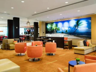 Modern lobby with orange and beige seating, palm tree wall art, and a small counter.