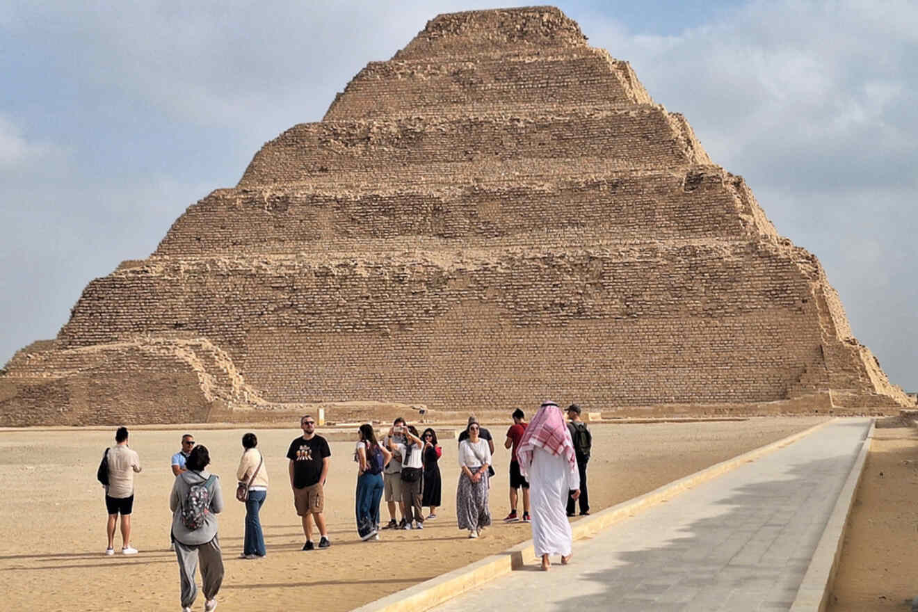 Tourists gather near the Step Pyramid of Djoser in Egypt under a cloudy sky.