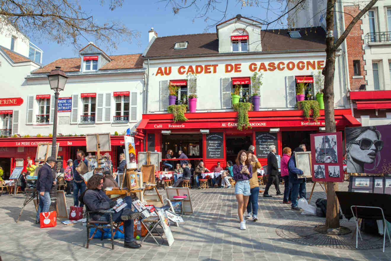 People gather in a vibrant street square with cafes, artists, and colorful buildings, Place du Tertre