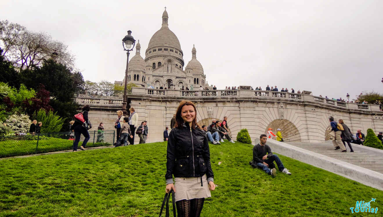 The writer of the post stands on a grassy area with the Sacré-Cœur Basilica in the background. People are sitting and walking nearby.