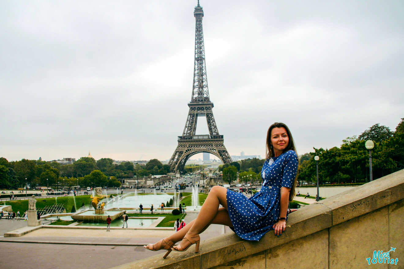 The writer of the post in a blue polka dot dress sits on a ledge with the Eiffel Tower in the background. The scene includes trees, fountains, and a cloudy sky.