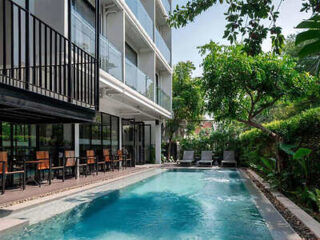 Modern building exterior with a rectangular swimming pool and lounge chairs, surrounded by greenery.