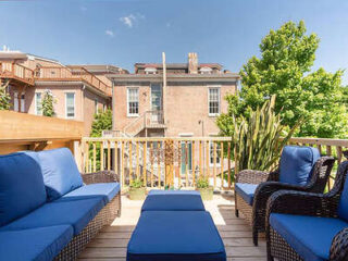 Rooftop deck with blue-cushioned wicker furniture, overlooking a brick building and greenery under a clear sky.