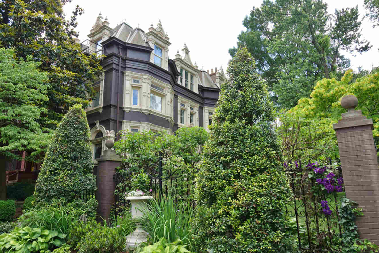 A historic, ornate building with multiple turrets is surrounded by lush greenery and manicured shrubs.