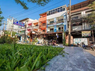 Street view of a row of colorful buildings with shops on the ground floor, motorbikes parked in front, and grass in the foreground under a clear blue sky.