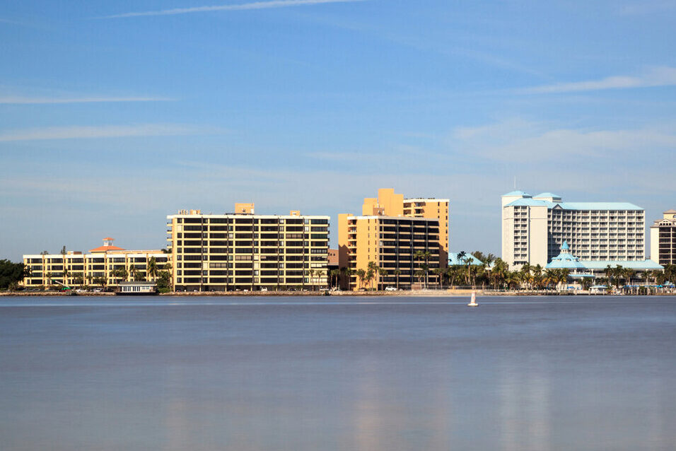 View of a calm body of water with several modern high-rise buildings in the background under a clear blue sky.