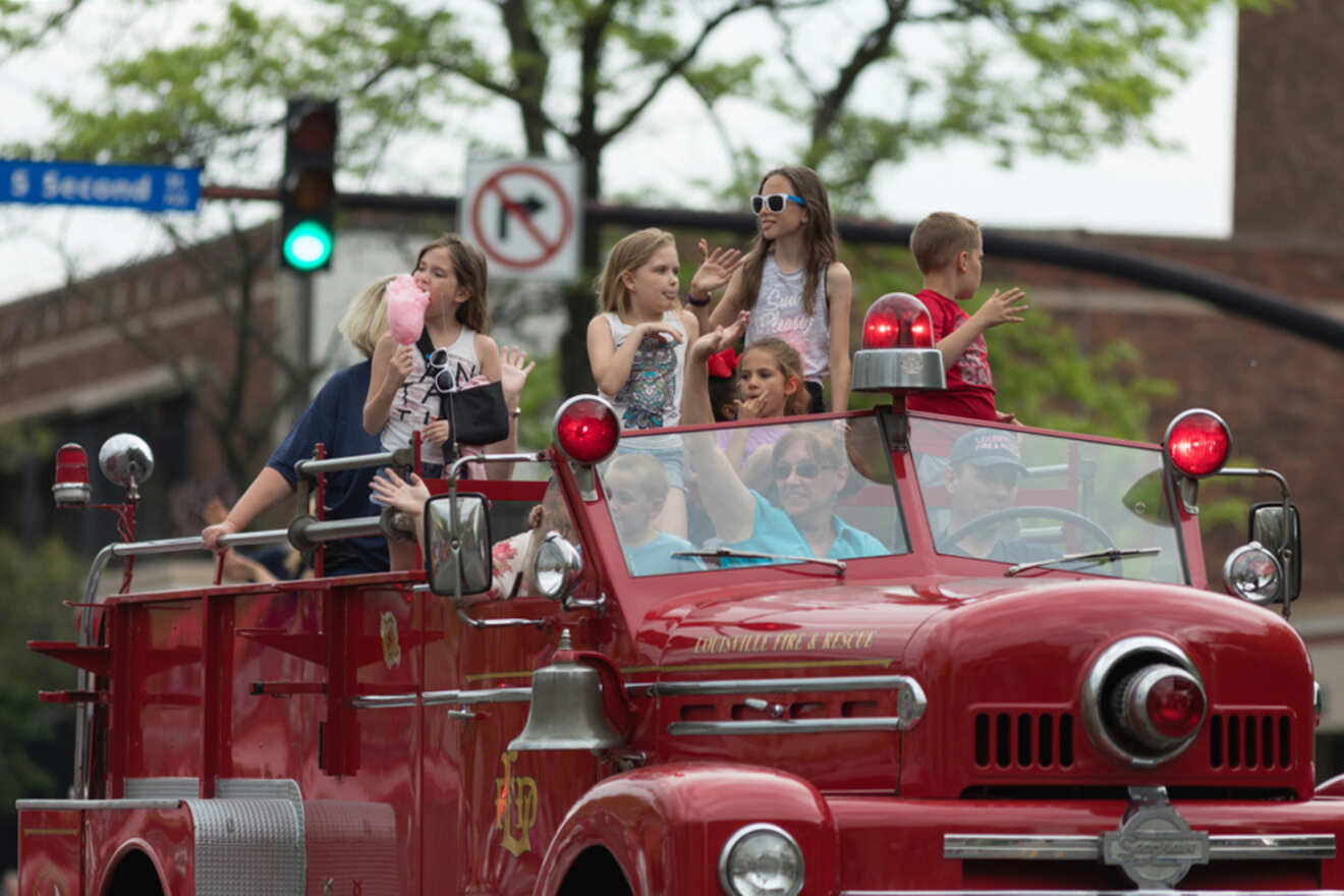 Children riding on an antique red fire truck during a parade.