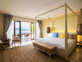 Spacious bedroom with a four-poster bed, soft lighting, and a view of the sea through open balcony doors.