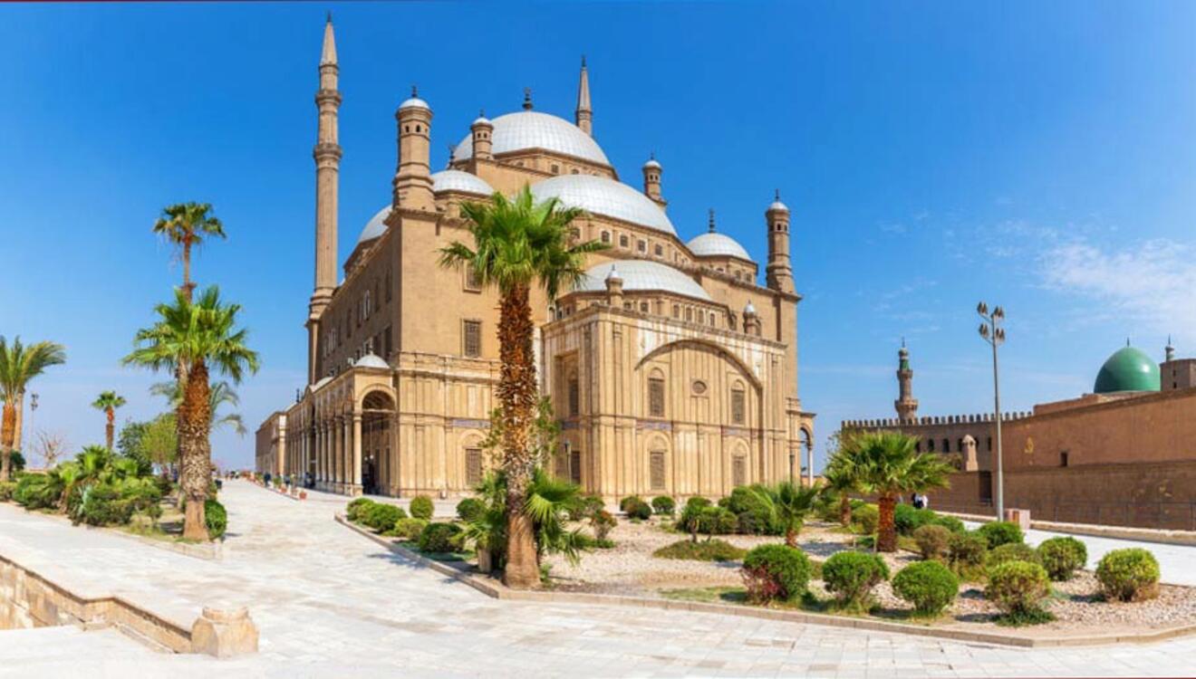 A mosque with large domes and minarets surrounded by palm trees under a clear blue sky.