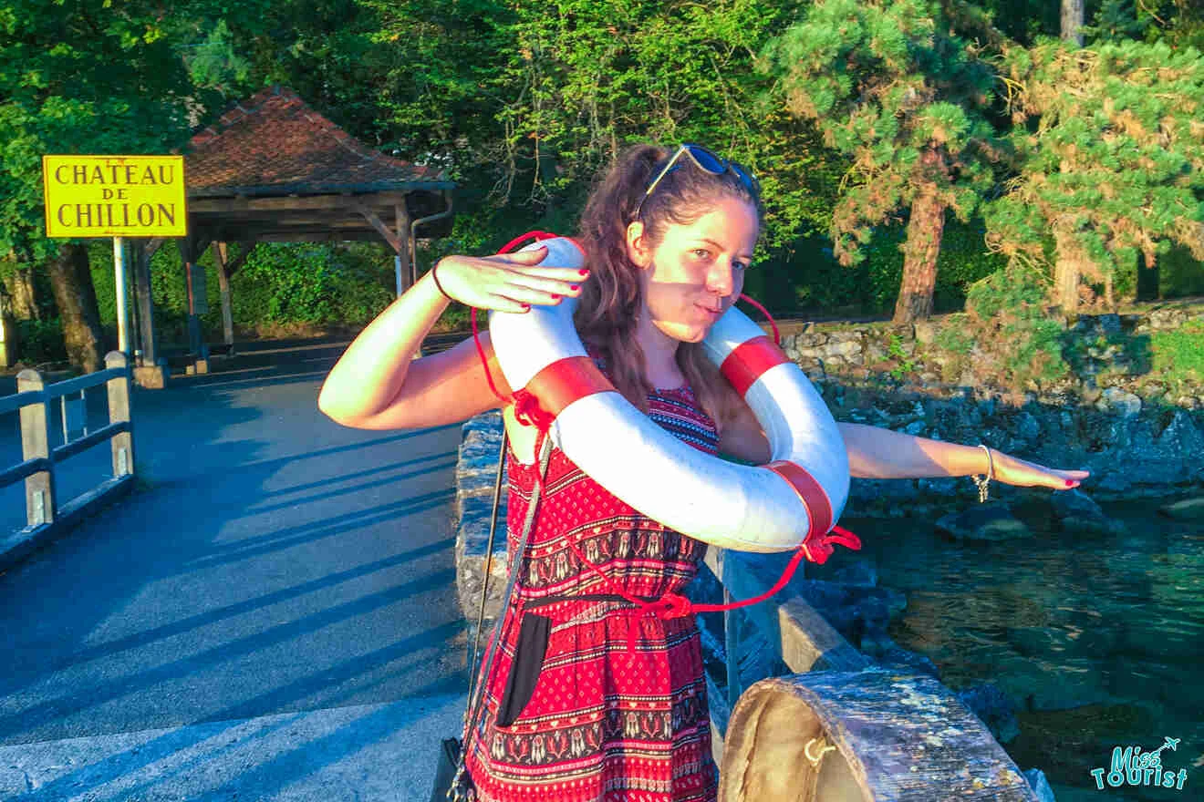 The writer of the post playfully poses with a lifebuoy on a path near Château de Chillon, surrounded by greenery and water.