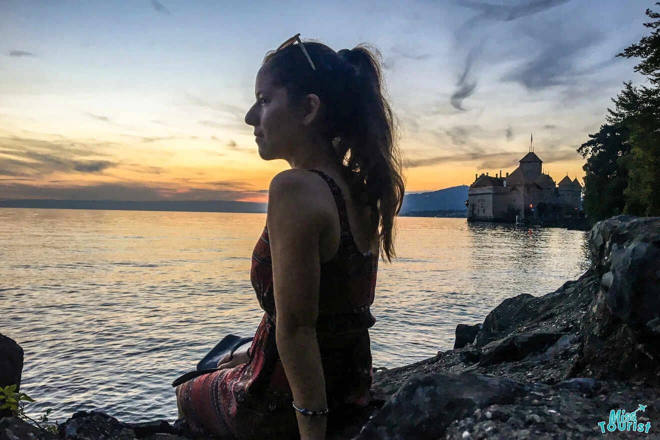 The writer of the post sits on a rocky shore overlooking a lake at sunset, with a castle in the background under a cloudy sky.