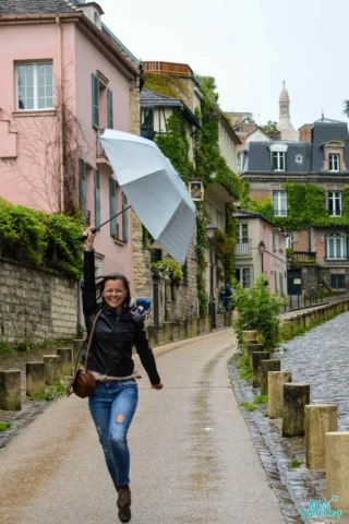 The writer of the post joyfully runs with an inverted white umbrella on a charming street in Montmartre lined with ivy-covered buildings.