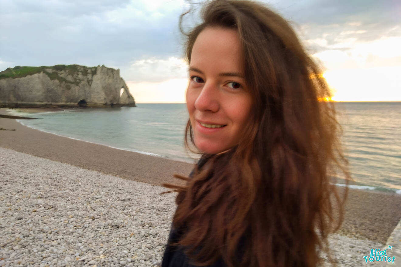 The writer of the post with long hair smiling on a rocky beach near cliffs at sunset in Normandy