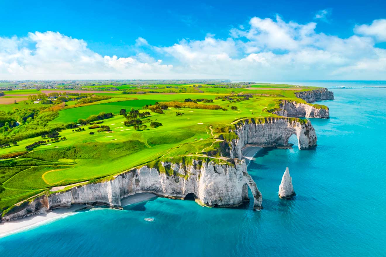 Aerial view of the white chalk cliffs and arches of Étretat, France, with green fields and blue sea.