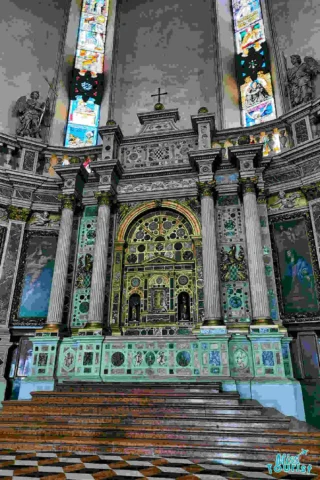 Ornate church altar featuring intricate mosaic designs, tall marble columns, stained glass windows, and religious statues on either side.